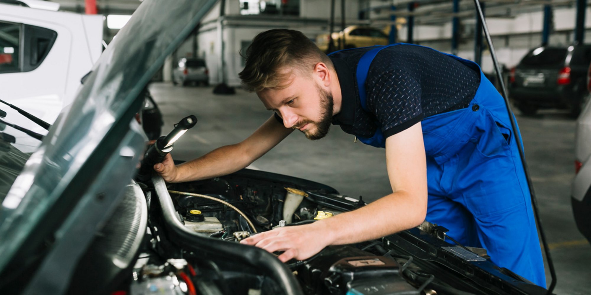 Mechaniker inspiziert konzentriert den Motorraum eines Fahrzeugs in der Werkstatt.